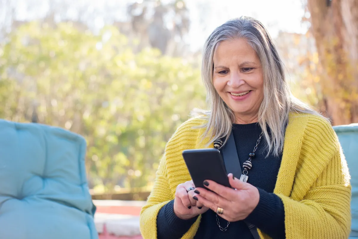 Femme âgée souriante écrivant un message sur son smartphone en extérieur